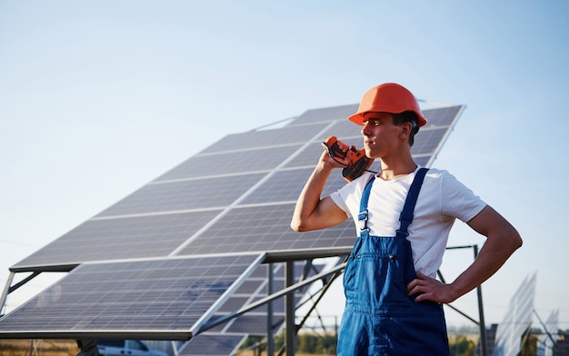 Destornillador inalámbrico en mano. Trabajador de sexo masculino en uniforme azul al aire libre con baterías solares en un día soleado.