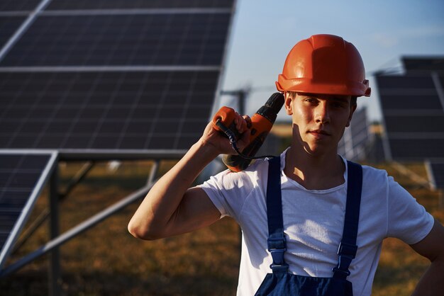 Con destornillador inalámbrico. Trabajador de sexo masculino en uniforme azul al aire libre con baterías solares en un día soleado.