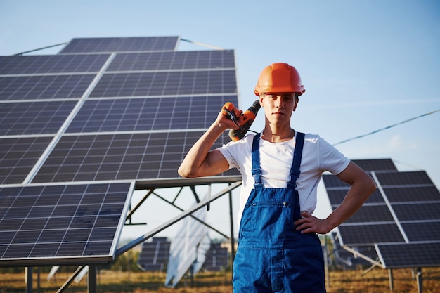 Destornillador inalámbrico. Trabajador de sexo masculino en uniforme azul al aire libre con baterías solares en un día soleado.