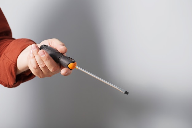 Destornillador en la mano de un hombre sobre un fondo de pared gris