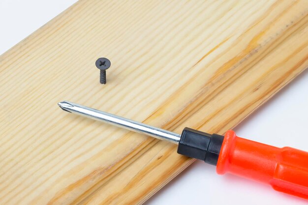 Destornillador y tornillo atornillado en una tabla de madera Sobre un fondo blancoCerrar