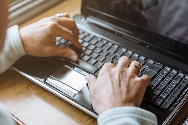 Detail der Hände des älteren Mannes, die an dem Laptop arbeiten