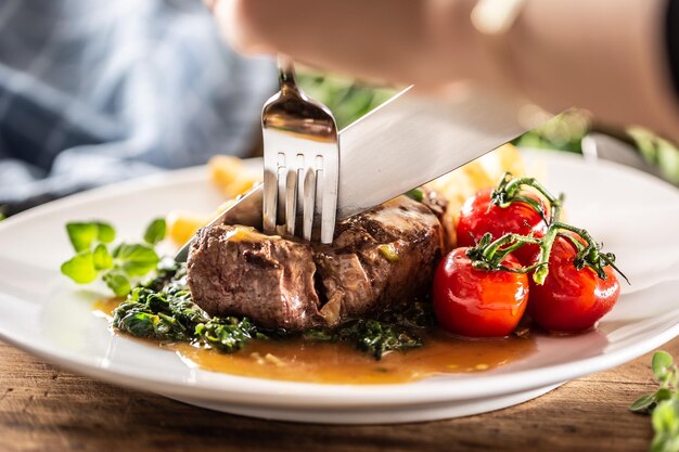 Detail einer Gabel und eines Messers, die in ein saftiges, perfekt gemachtes Steak auf einem Teller schneiden