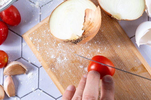 Detail einer handschneidenden Tomate zwischen Zutaten und Küchenwerkzeugen