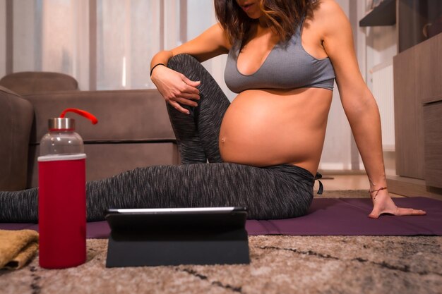 Detail einer jungen schwangeren kaukasischen Frau mit grauem T-Shirt, die Pilates-Übungen durchführt Online-Übungen in Prepartum-Kursen Wellness während der Schwangerschaft