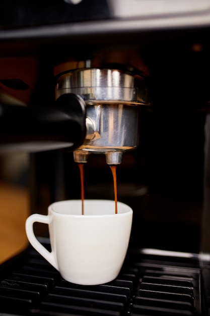 Detail einer professionellen kaffeemaschine, die in einer cafeteria kaffee in eine leere tasse tropft. die maschine macht einen perfekten kaffee mit köstlichem geruch. espresso-kaffeemaschine espresso-kaffee zubereiten