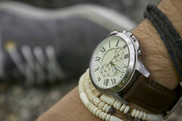 Detail einer Vintage-Armbanduhr, die von einem Jungen mit anderen Armbändern getragen wird, Symbol der Zeit. Ein tolles Accessoire für ein perfektes Outfit.