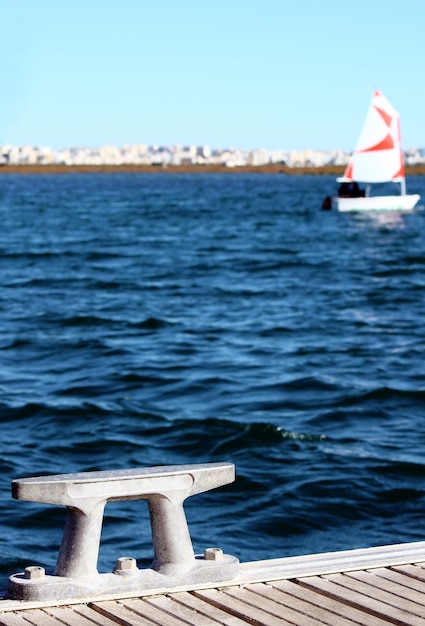 Detail eines modernen Ankerplatzes, auf dem Hintergrund ist ein kleines Segelboot und die Stadt unscharf.