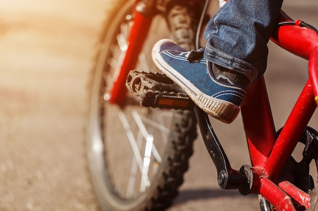 Detail von den Kinderradfahrerfüßen, die Fahrrad auf im Freien in der sonnigen Straße reiten. Nahaufnahme auf Pedal und Fuß