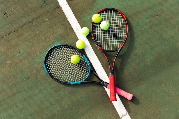 Detail von zwei Tennisschlägern und Tennisbällen, die auf dem Boden auf einem Tennisplatz im Freien liegen. Sport, gesunde Hobbys, Wettkampf, Fitness und Freizeitkonzept.