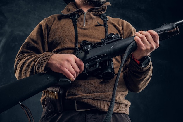 Foto detailansicht auf hände mit gewehr. studiofoto eines jägers vor dunklem wandhintergrund