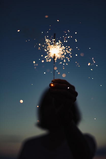 Foto detailansicht der hand, die brennende wunderkerze in der abenddunkelheit hält