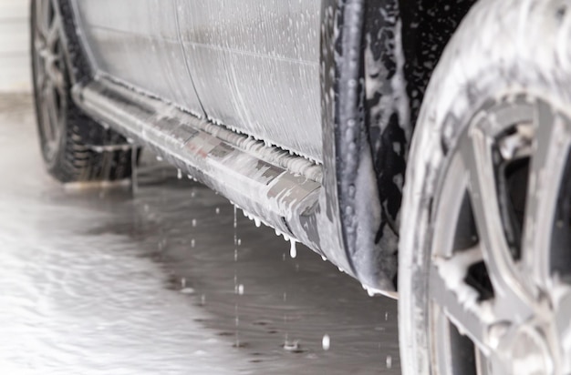 Detailansicht der silbernen Autostufe in der Autowaschanlage mit Seifenschaumflecken und Tropfen