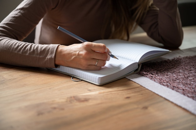 Detailansicht einer Frau, Student, Schreiben in leeres Notizbuch beim Lernen von zu Hause aus.