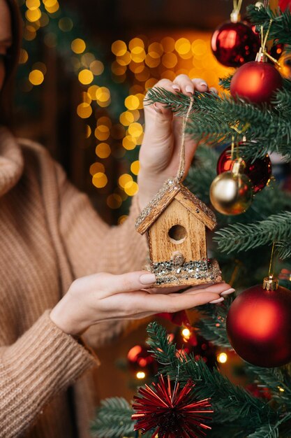 Detailansicht einer nicht erkennbaren Frau, die Weihnachtsspielzeug auf dem Hintergrund des Weihnachtsbaums hält