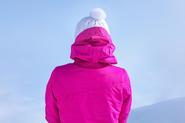 Detailansicht von hinten zur jungen Frau in rosa Skijacke, die oben auf dem Berg steht.