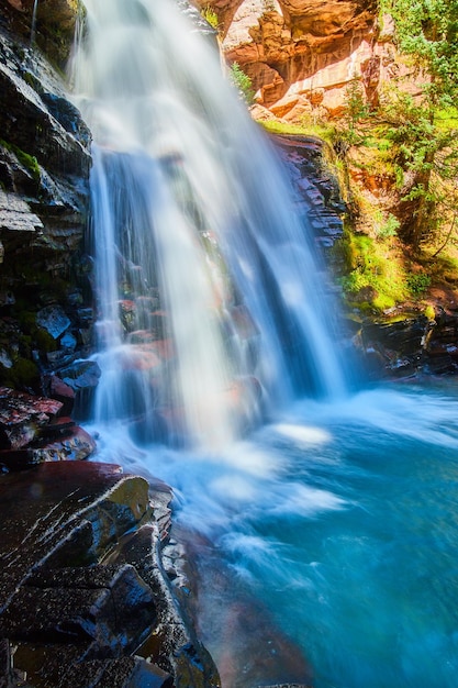 Detailbild des Wasserfalls über Klippen mit roten Felsen und Moos in blauen Eimer Wasser