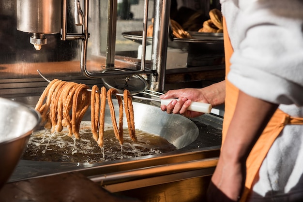 Detailfoto eines Arbeiters, der die Churros aus dem heißen Öl nimmt, bereit, auf der Straße serviert zu werden