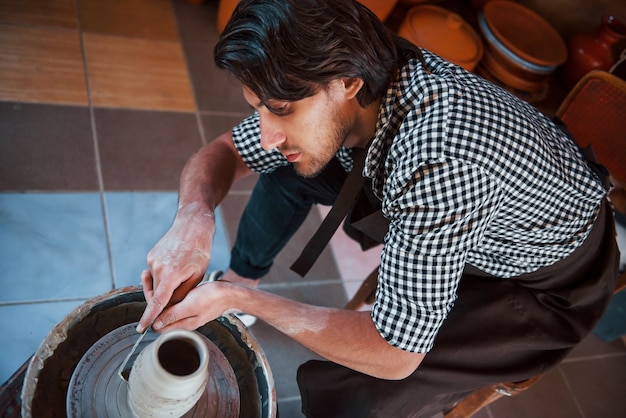 Detaillierung durch Spezialwerkzeug. Ceramist verwendet Töpferscheibe und stellt ein handgefertigtes Tonprodukt her.