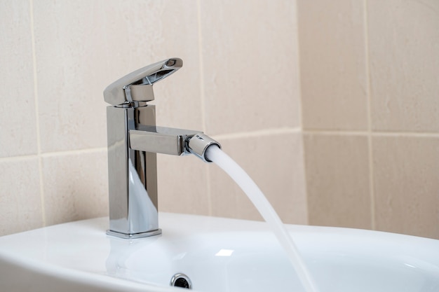 Details des weißen Keramikbidet mit Wasser, das vom Wasserhahn im modernen Badezimmer mit beige Fliesen läuft