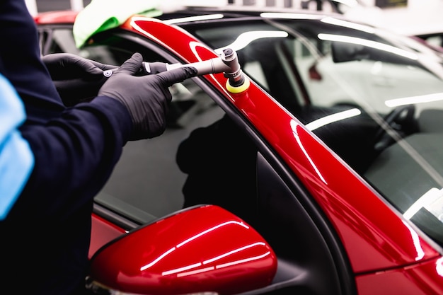 Detalhamento de carro - Homem com polidor orbital em oficina de polimento de carro. Foco seletivo.