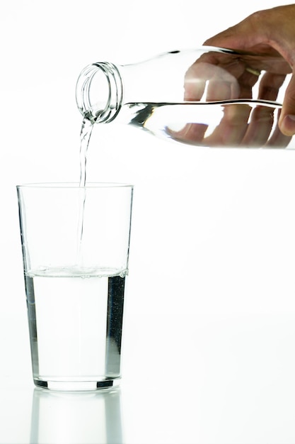 Detalhe da mão de um homem irreconhecível derramando água em um copo de cristal em um fundo branco