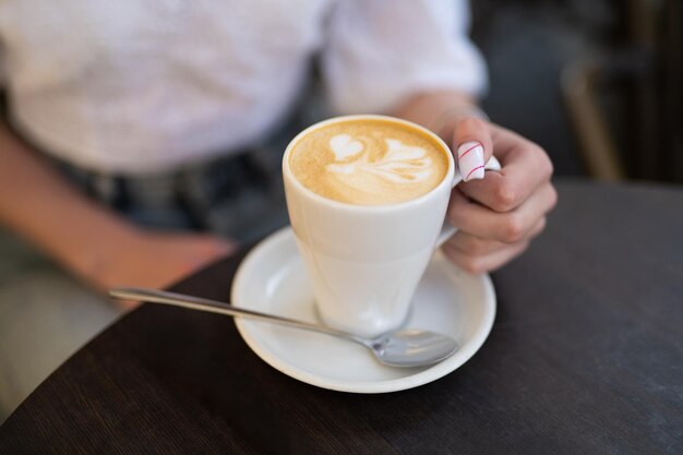 Foto detalhe da mão de uma garota segurando uma xícara de café em uma mesa em um café