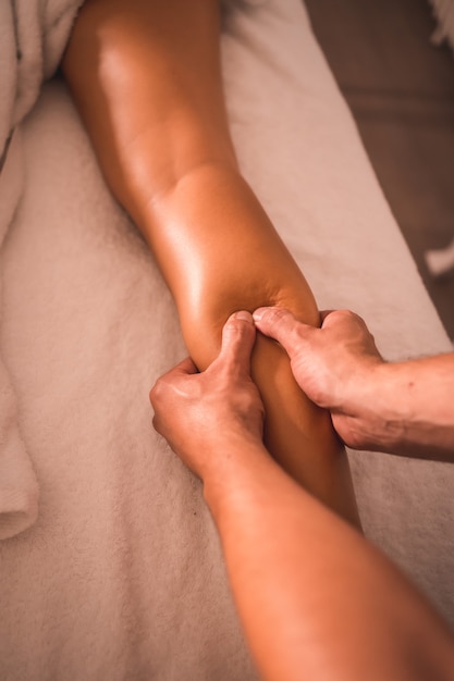 Foto detalhe da massagem de um fisioterapeuta nas costas da perna direita de uma jovem deitada sobre a mesa. fisioterapia, osteopatia, massagem relaxante, movimento vídeo de tratamento nas costas