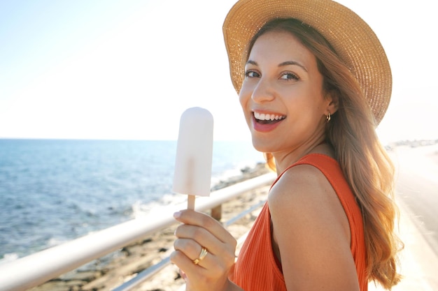 Detalhe da mulher brasileira rindo comendo um picolé de limão olhando para a câmera no verão