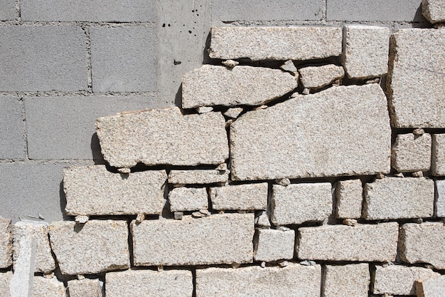 Detalhe da parede de blocos de concreto sendo revestida com lajes de pedra de granito no canteiro de obras ao ar livre