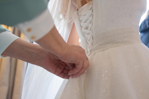 Detalhe das mãos das damas de honra puxando a fita de saciedade do espartilho do vestido de noiva da noiva durante o vestir