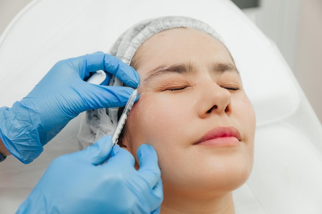 Detalhe das mãos de uma esteticista injetando Botox na testa de uma mulher Correção de rugas na testa e nos olhos com toxina botulínica
