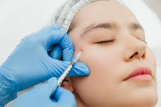 Detalhe das mãos de uma esteticista injetando Botox na testa de uma mulher Correção de rugas na testa e nos olhos com toxina botulínica