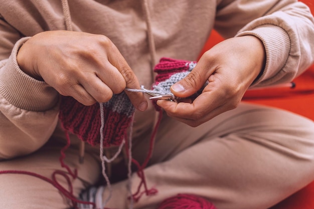 Detalhe das mãos de uma mulher tricotando lã com agulhas