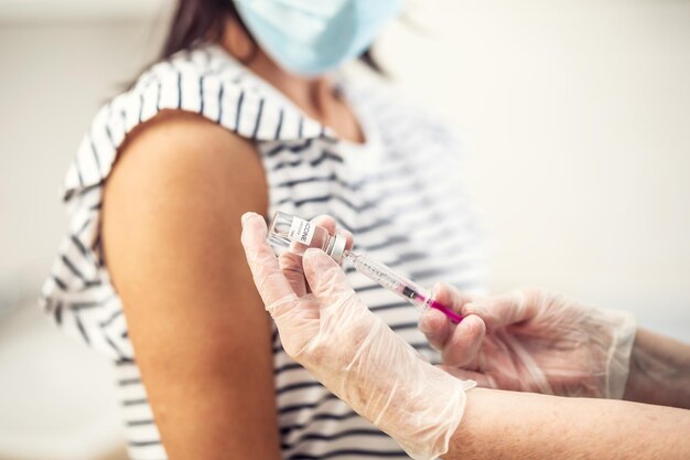 Detalhe das mãos do médico tomando uma dose da vacina Covid-19 em uma paciente esperando a vacinação.