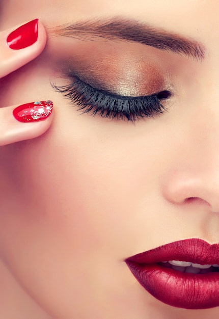 Detalhe de close-up do rosto feminino revela olhos fechados cobertos por pálpebras coloridas com maquiagem esfumada, sobrancelha bem formada e lábios vermelhos brilhantes. produtos de maquiagem, manicure e cosméticos.