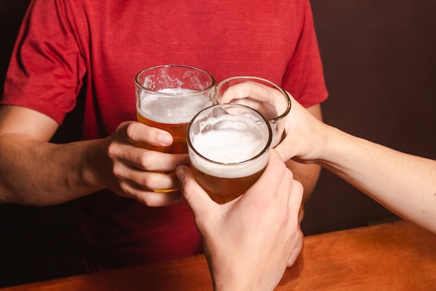 Detalhe de gente batendo os copos de cerveja no bar.