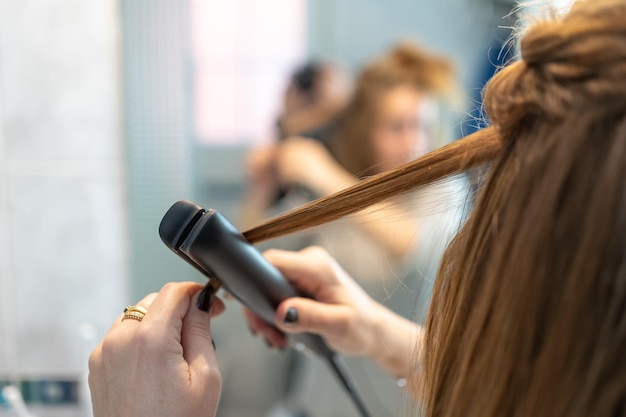 Detalhe de um alisador de cabelo sendo usado por uma mulher na frente do espelho em seu banheiro