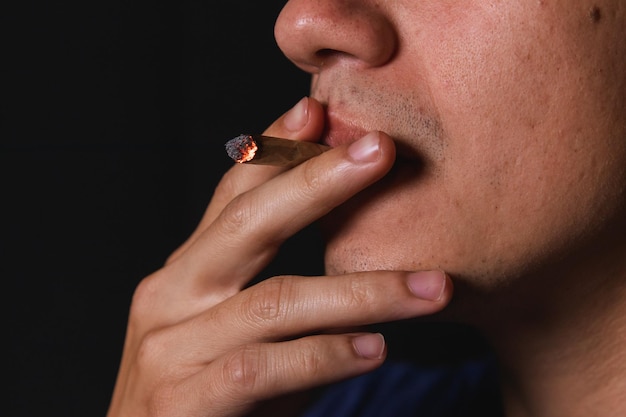 Detalhe de um homem fumando um baseado em um fundo preto