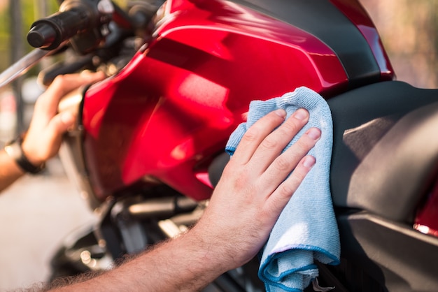 Detalhe de um homem limpando e secando sua motocicleta com um pano de microfibra do lado de fora.