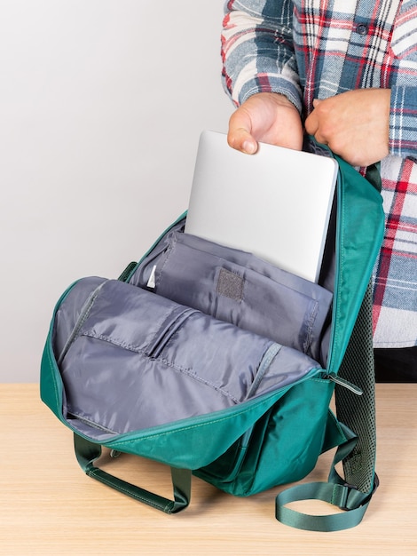 Foto detalhe de um jovem estudante do sexo masculino tirando um laptop de uma mochila