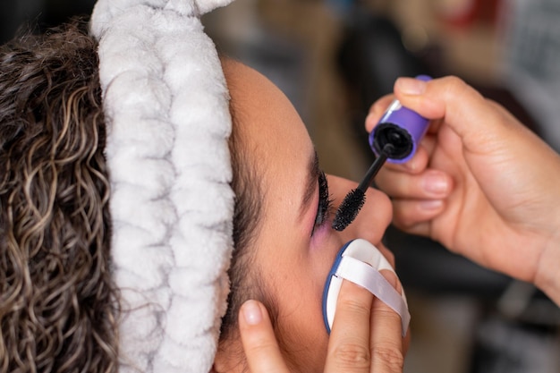 Detalhe de um maquiador profissional aplicando rímel nos cílios de uma mulher