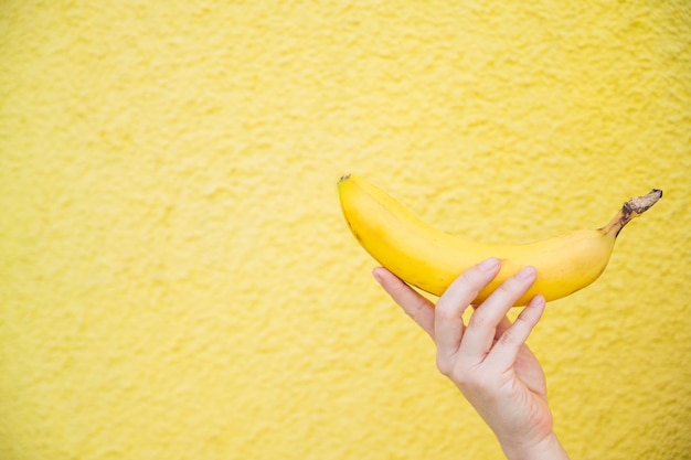 Detalhe de uma banana em uma mão feminina em um fundo amarelo