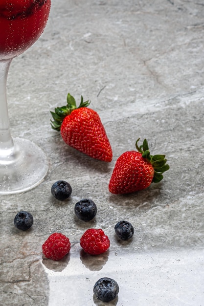 Detalhe de uma bebida servida com frutas, morango e mirtilo com gin e gelo