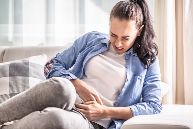 Detalhe de uma mulher com dores abdominais, vesícula biliar, ovários, apêndice, fígado ou intestinos segurando a barriga com as mãos.