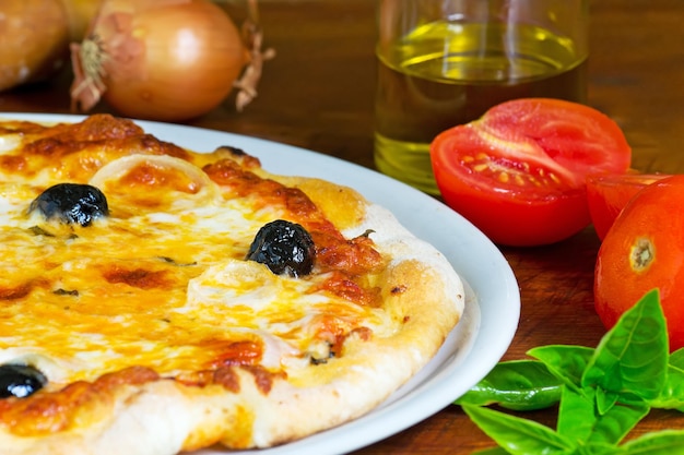 Detalhe de uma pizza em uma mesa de madeira com ingredientes ao redor