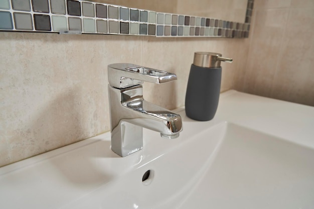 Detalhe de uma torneira de banheiro prateada e dispensador de sabão