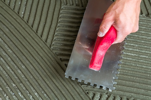 Detalhe do close-up de instalação de ladrilhos. Melhoria home, renovação. Mão de trabalhadores com flutuador entalhado para azulejo. Adesivo para pavimentos em cerâmica, argamassa.