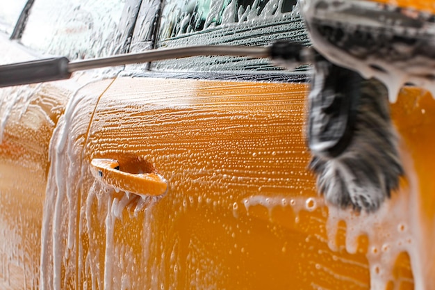 Detalhe do lado do carro amarelo escuro lavado no lava-jato. Escove deixando traços em espuma de sabão branco e xampu.