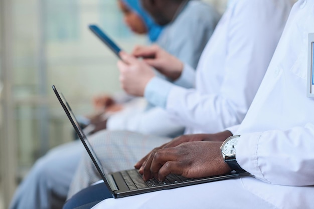 Detalhe do médico afro-americano em jaleco branco digitando no laptop na conferência